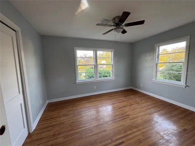 an empty room with wooden floor fan and windows