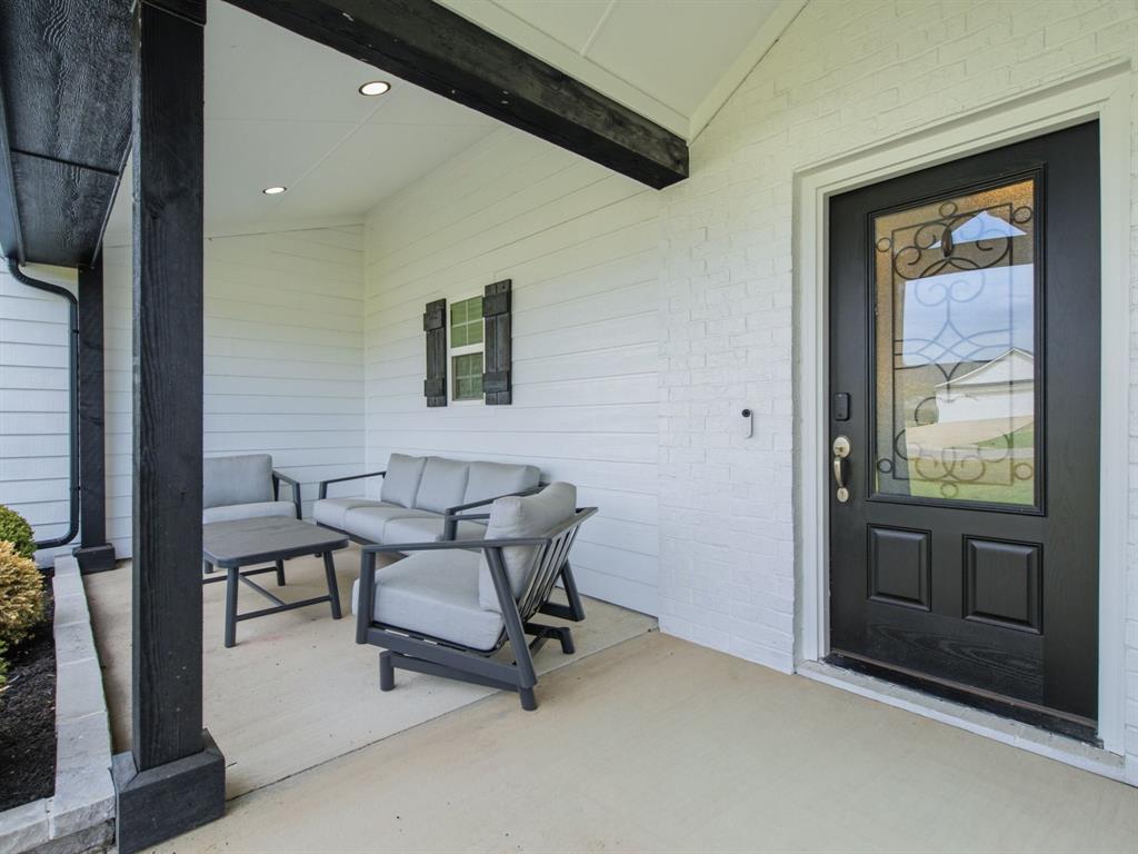 10216 Finch Road Sanger, TX 76266 - Photo 5 of 40 Covered front porch featuring a dark-stained wood beam and columns, white brick and siding exterior, recessed lighting, and a dark-paneled entry door with decorative glass