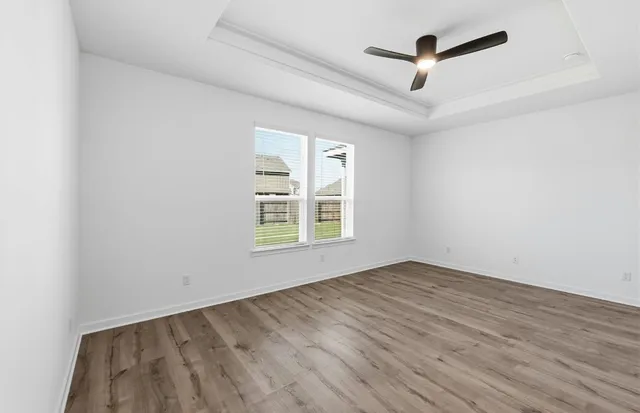 an empty room with wooden floor ceiling fan and windows