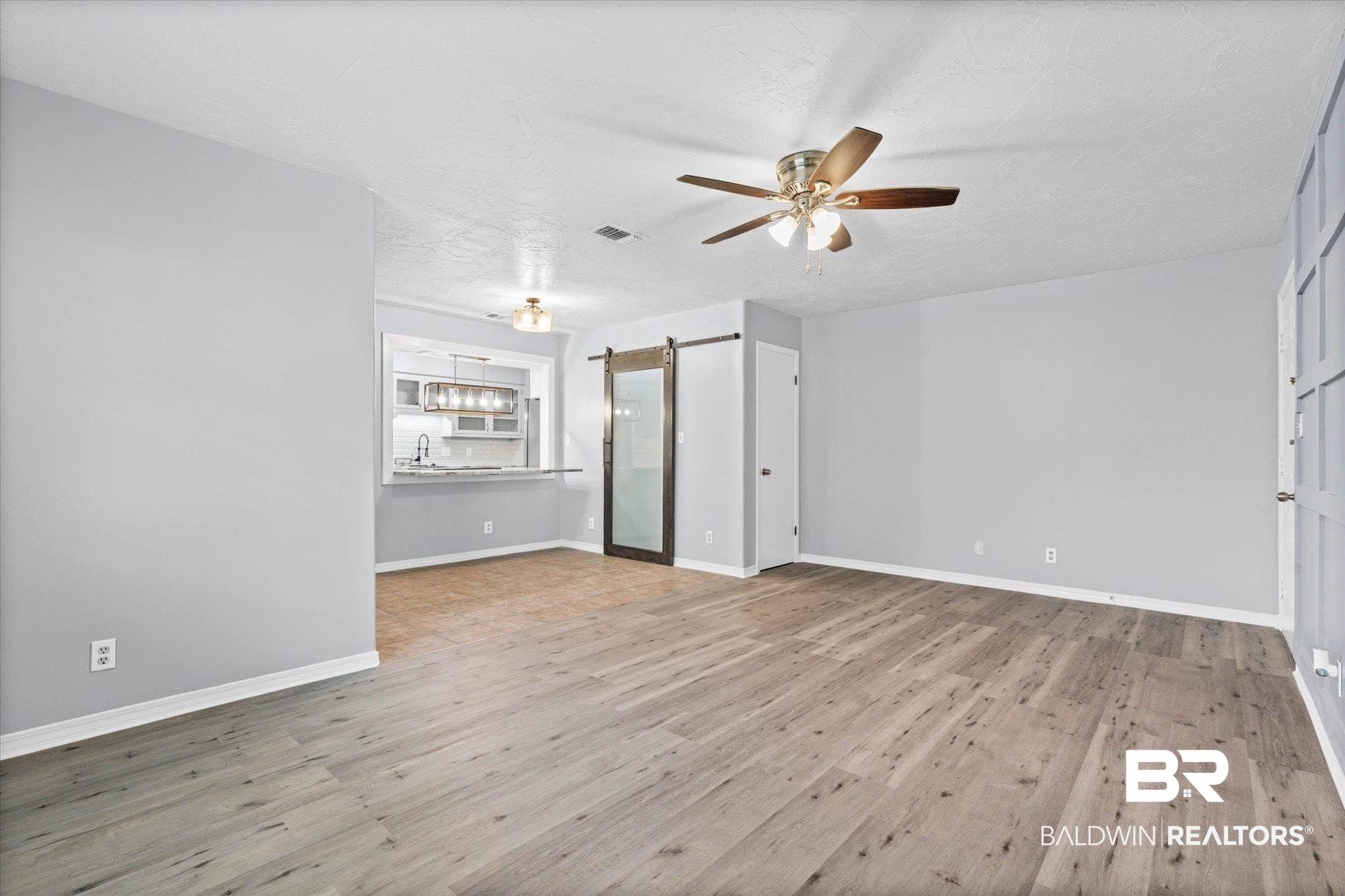 500 Grant Street, Unit C210 Daphne, AL 36526 - Photo 5 of 26 Spacious interior featuring wood-finish flooring, a contemporary ceiling fan, and a pass-through window to the kitchen with an industrial-style light fixture