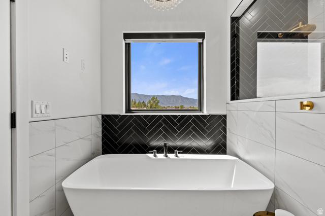 3111 South 1250 West Logan, UT 84321 - Photo 19 of 51 Freestanding soaking tub with mountain scenery through a picture window, complemented by black herringbone tile and white marble-look wall tiles