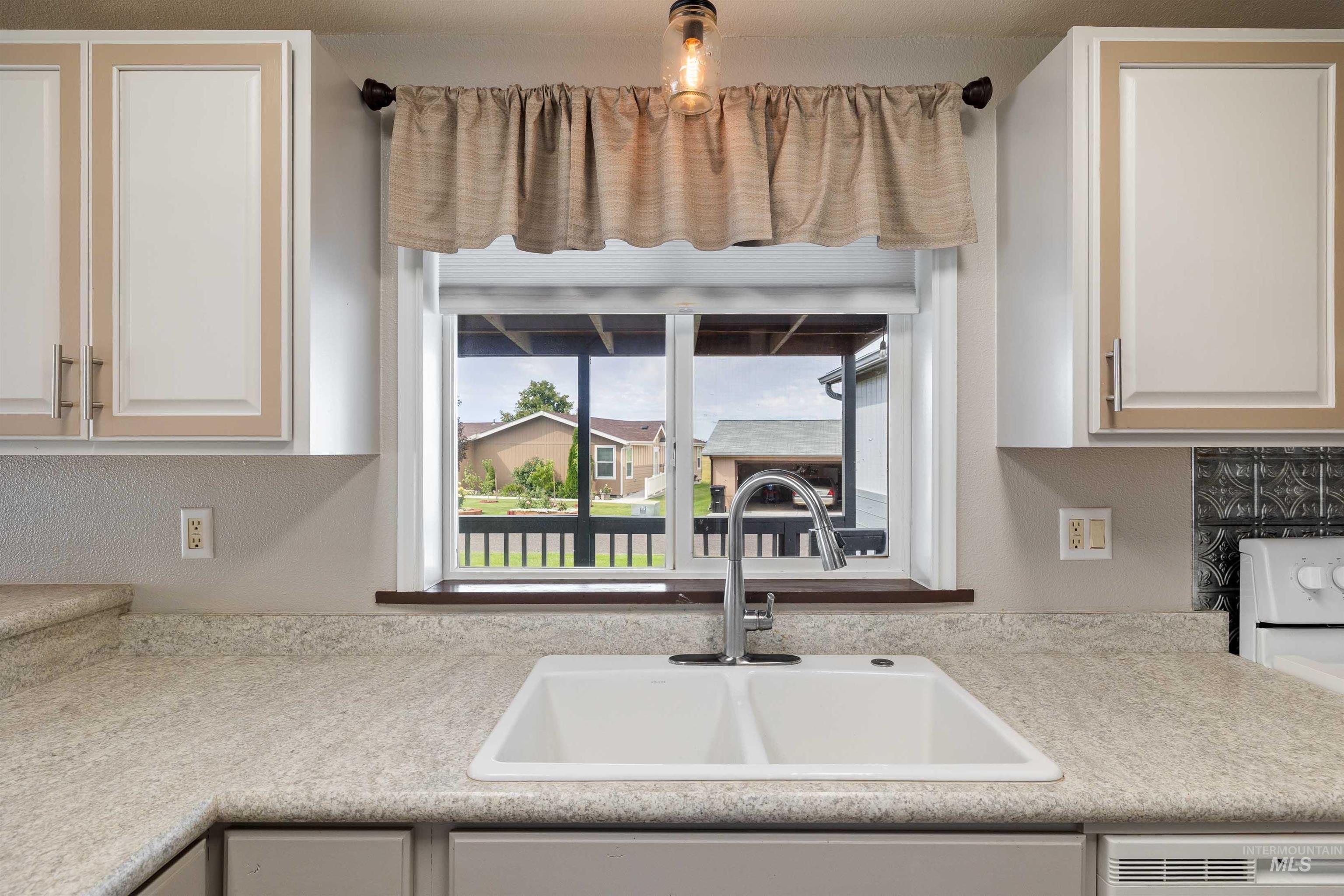 910 Moonglo, Unit 80 Buhl, ID 83316 - Photo 9 of 25 Kitchen sink area featuring a double basin sink with a chrome faucet, light speckled countertops, and upper cabinetry with framed doors