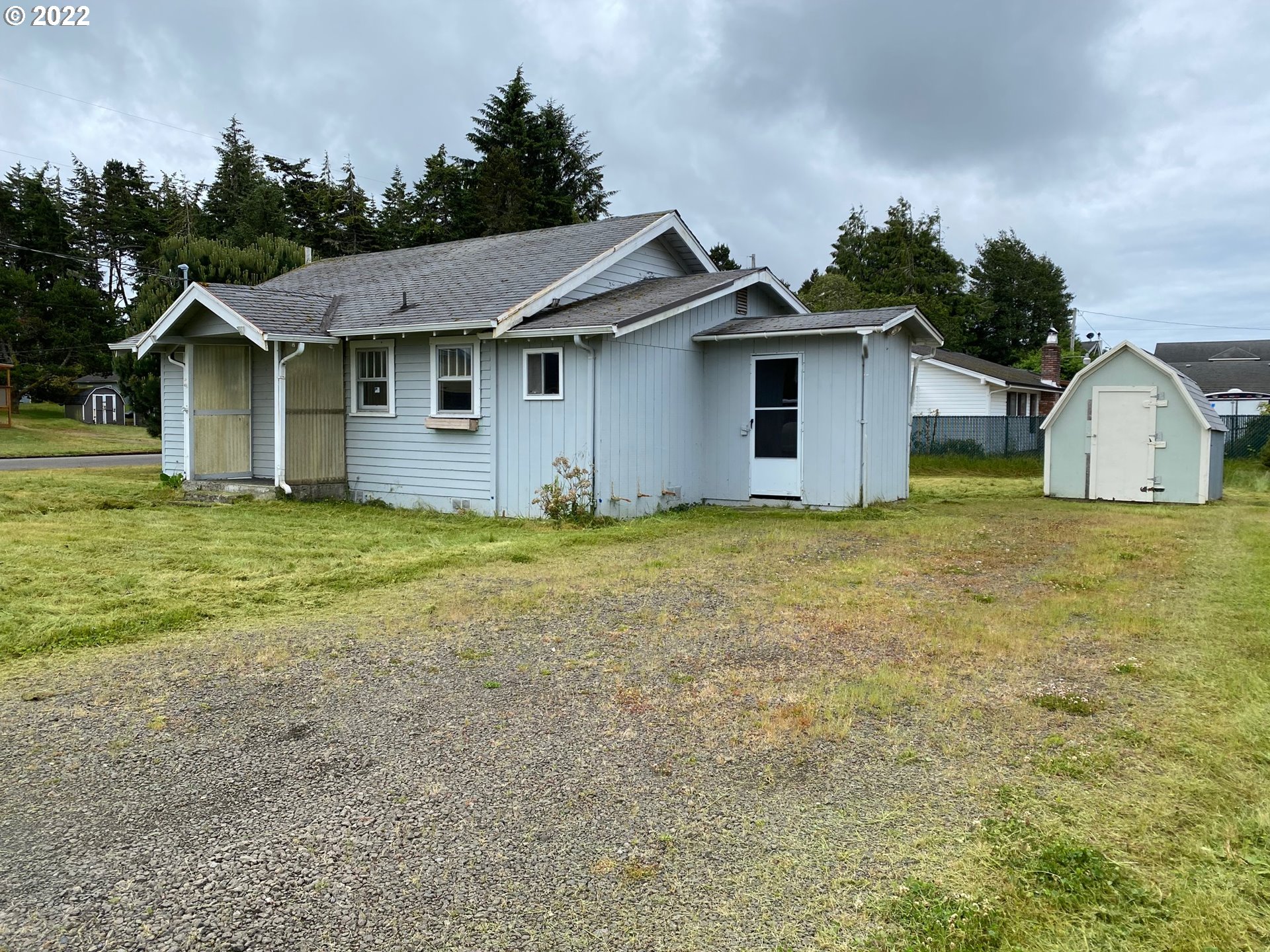 1184 2nd Street Florence, OR 97439 - Photo 2 of 4 a white house that has a big yard and large trees with wooden fence