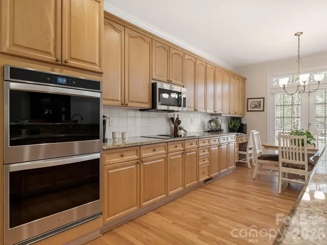 a kitchen with stainless steel appliances granite countertop a stove top oven a sink dishwasher a dining table and chairs with wooden floor