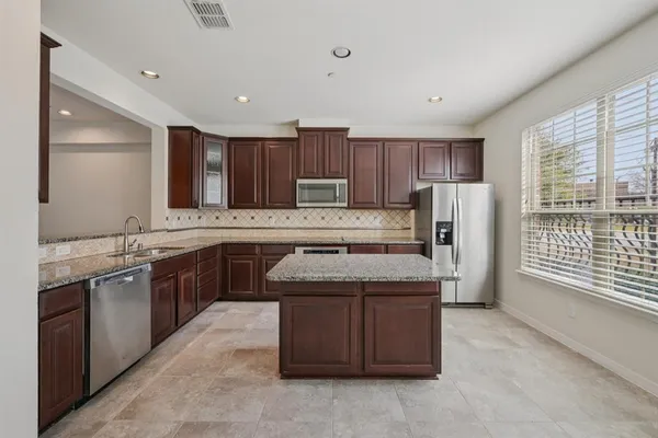 a kitchen with stainless steel appliances granite countertop a stove a refrigerator and a sink with wooden cabinets