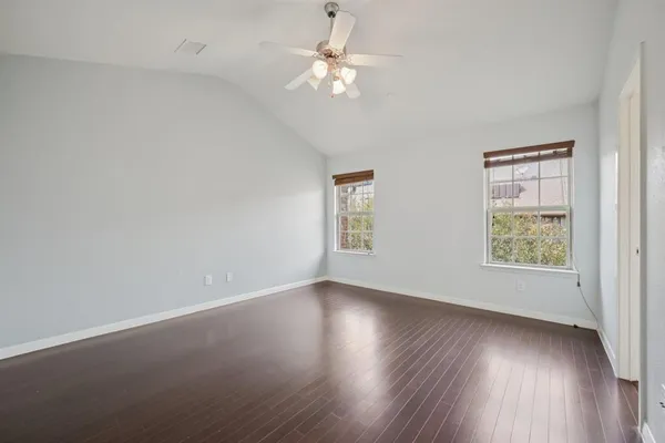 an empty room with wooden floor chandelier fan and windows