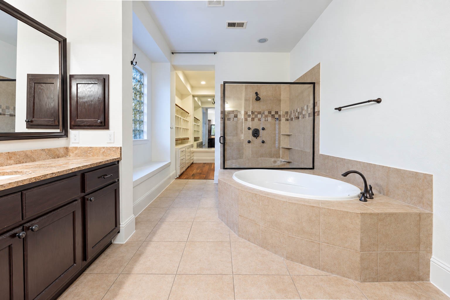 5403 Mesquite Ridge Street Fulshear, TX 77441 - Photo 22 of 42 A deep soaking tub with a neutral tile surround that coordinates with the flooring invites you to unwind, while a separate walk in shower offers a custom glass enclosure and dark finishes. A privacy window lets natural light in without sacrificing privacy.