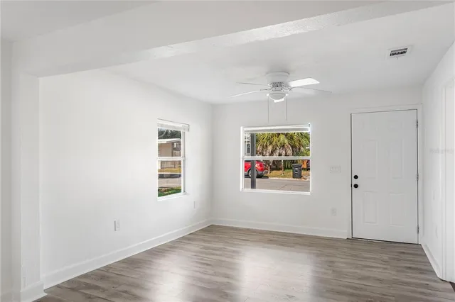 an empty room with wooden floor chandelier fan and windows