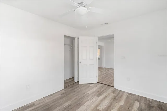 a view of an empty room with wooden floor and a ceiling fan