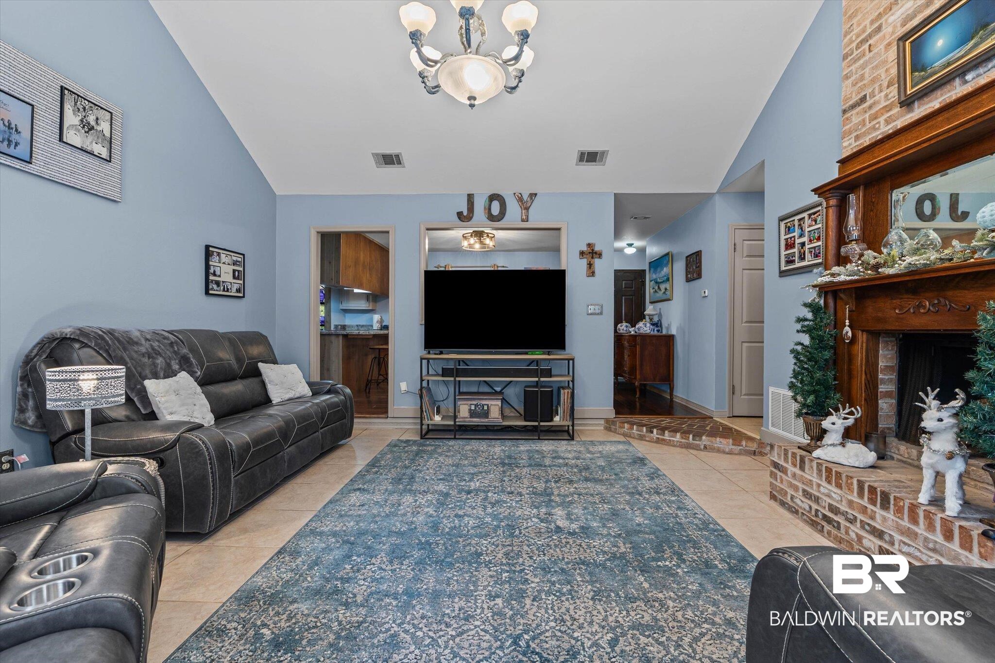 3846 Leslie Road Saraland, AL 36571 - Photo 7 of 40 Living area with lofted ceiling, light tile patterned floors, a brick fireplace, and a chandelier