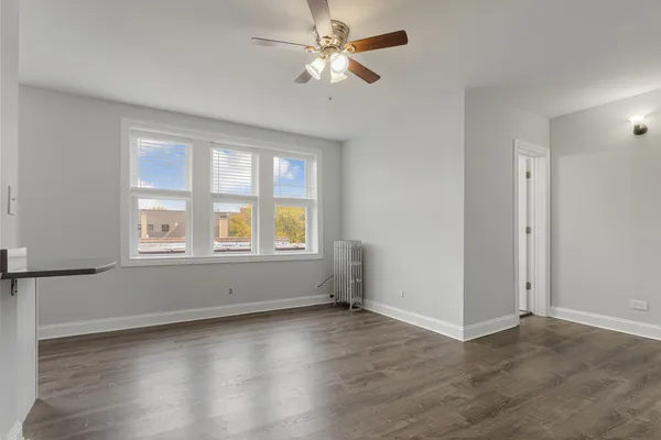 an empty room with wooden floor chandelier fan and windows