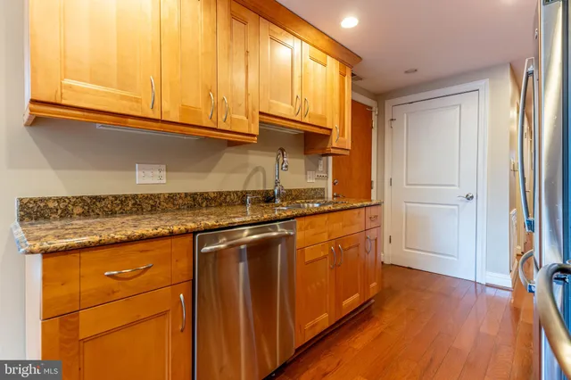 a kitchen with stainless steel appliances granite countertop a refrigerator a sink dishwasher and wooden cabinets with wooden floor