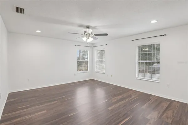 an empty room with wooden floor chandelier fan and windows