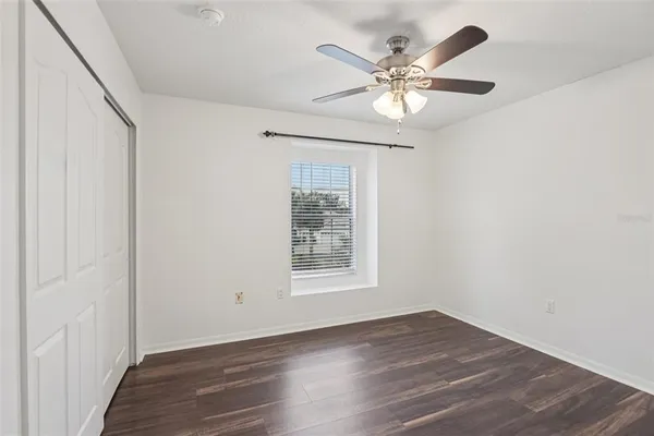 a view of an empty room with wooden floor and a ceiling fan