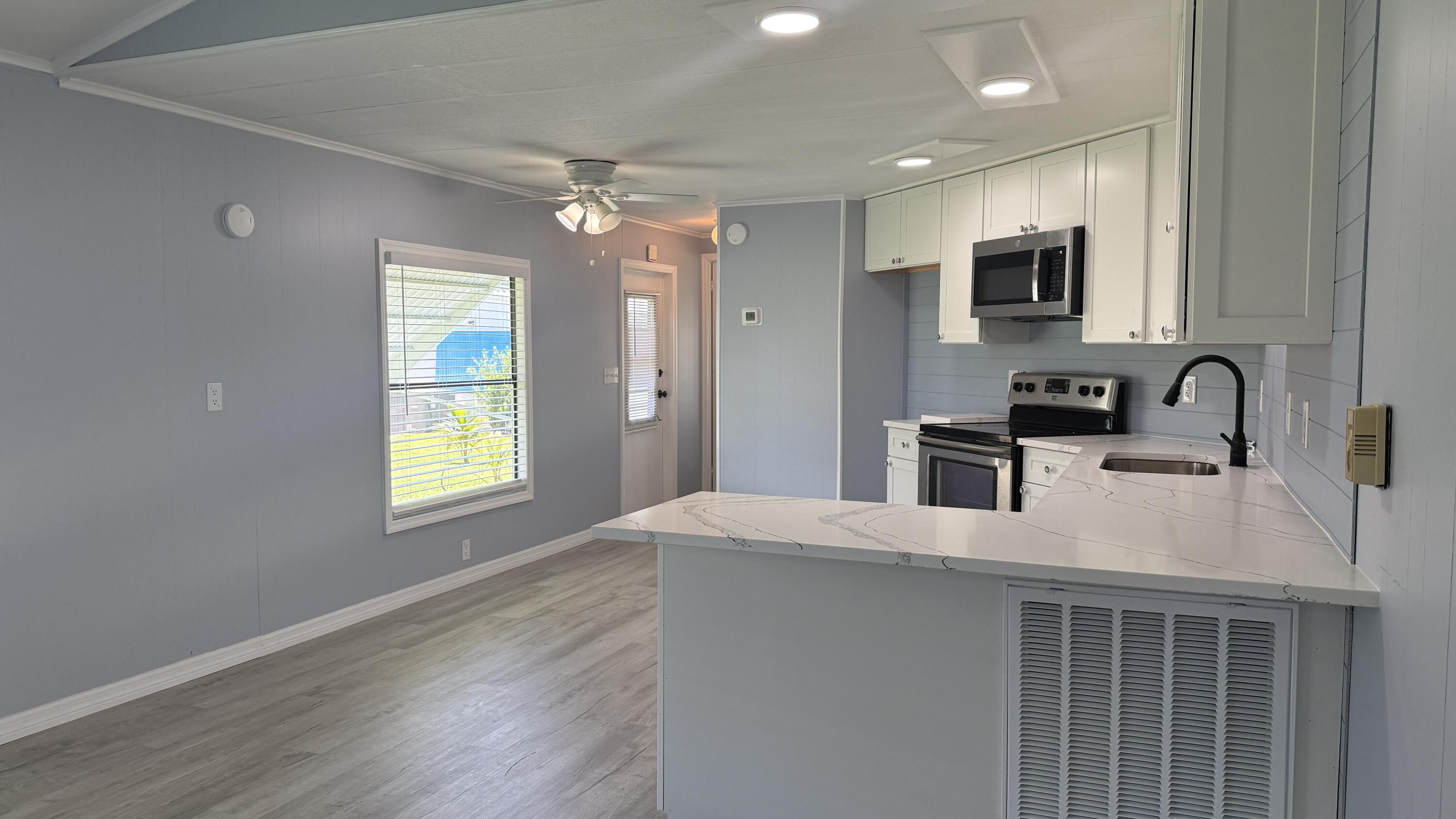 6919 Southeast Congress Street Hobe Sound, FL 33455 - Photo 7 of 52 a kitchen with stainless steel appliances a sink dishwasher a microwave oven a stove with white cabinets and wooden floor