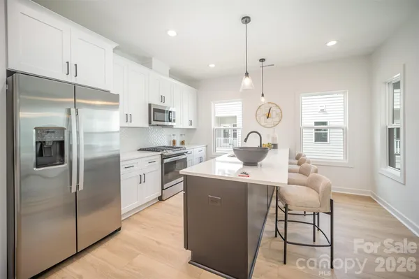 a kitchen with stainless steel appliances granite countertop a refrigerator a sink dishwasher a stove and white cabinets with wooden floor