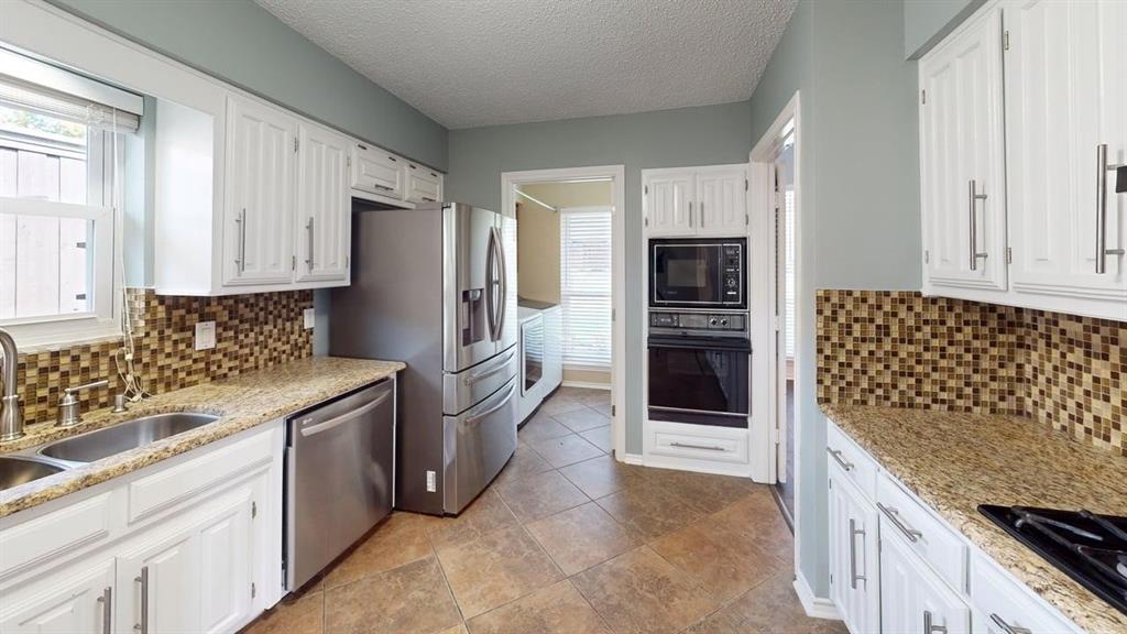White cabinetry with stainless steel appliances, granite countertops, mosaic tile backsplash, and tile flooring