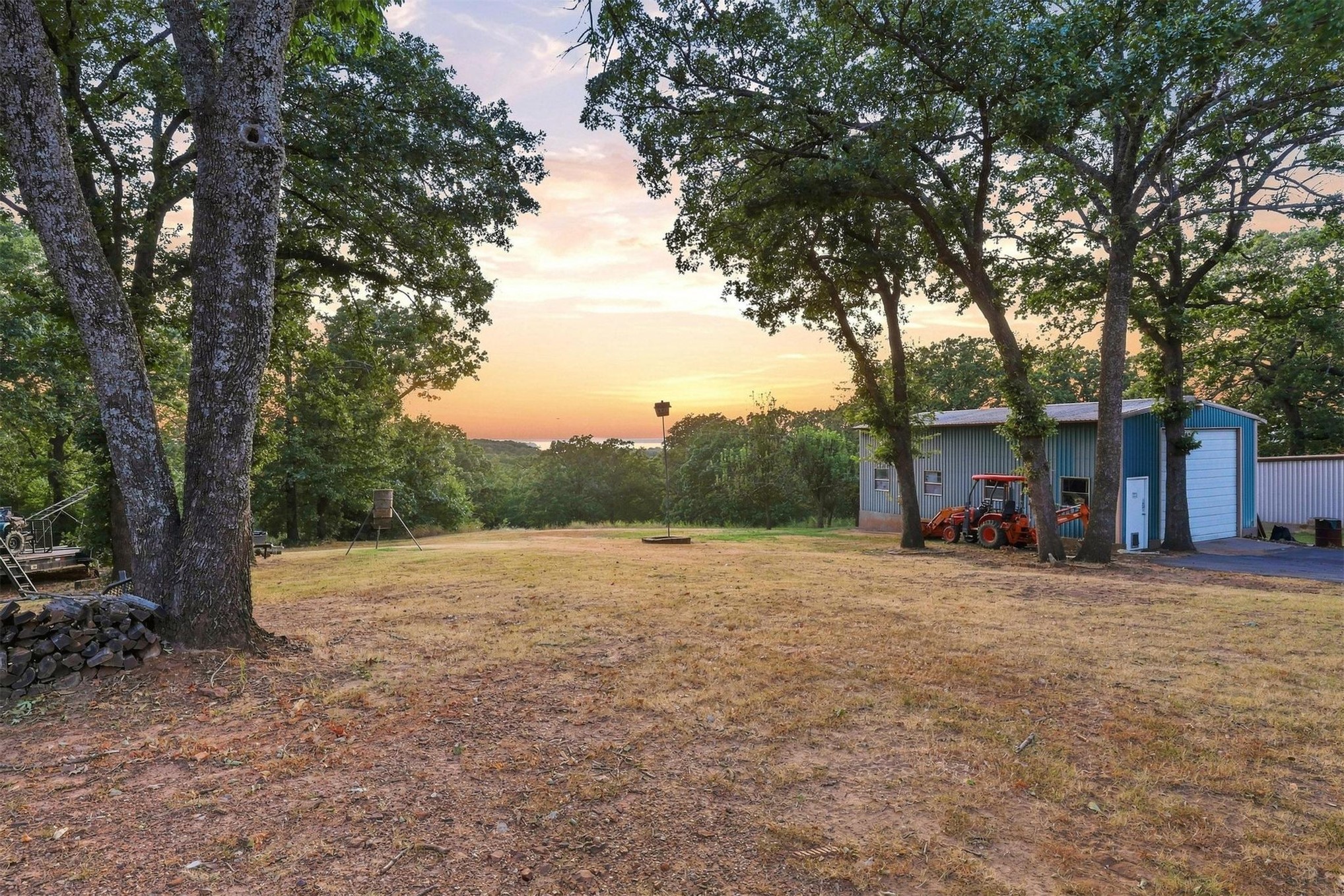 171 Woods Road Mead, OK 73449 - Photo 53 of 62 Expansive lot with mature trees, a metal building with garage doors, and a paved driveway