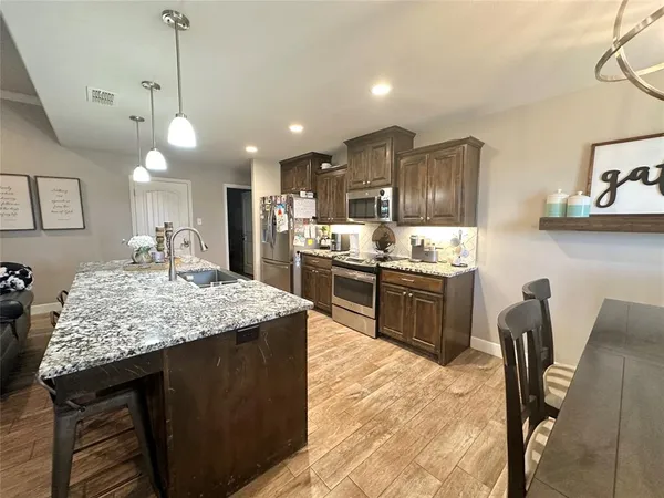 a kitchen with kitchen island a dining table chairs stainless steel appliances and cabinets