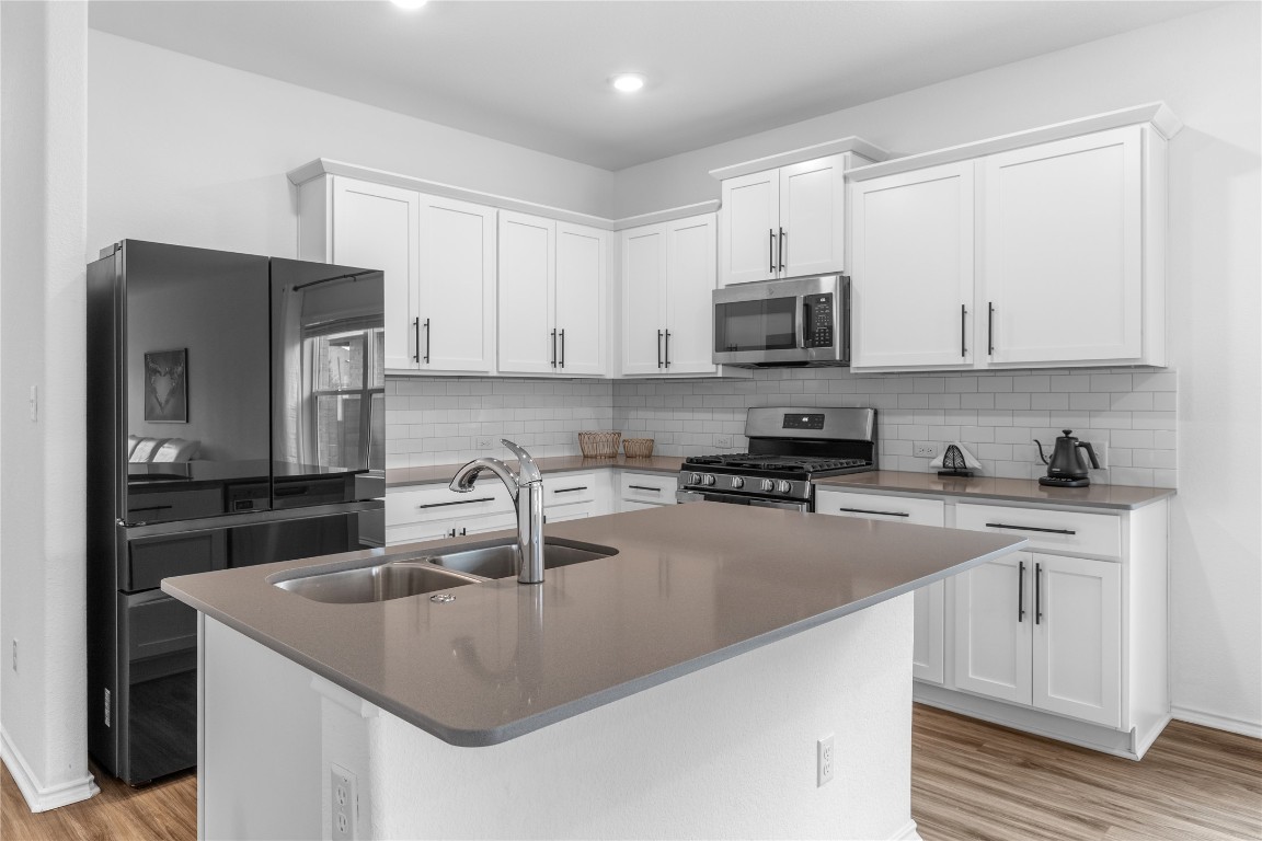 432 Clear Springs Road Georgetown, TX 78628 - Photo 3 of 27 Kitchen featuring white cabinets, appliances with stainless steel finishes, an island with sink, light wood-style flooring, and dark stone countertops