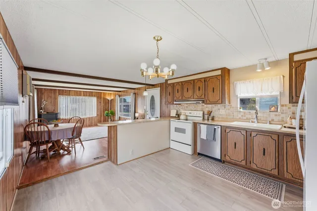 a large white kitchen with granite countertop a stove a sink a dining table and chairs with wooden floor