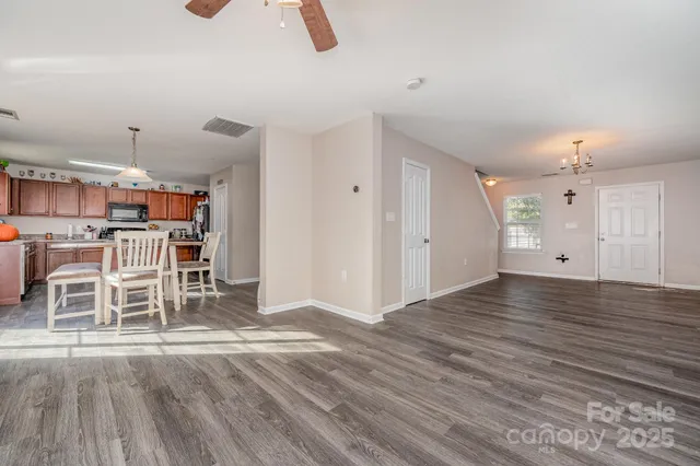 an empty room with wooden floor and way to kitchen