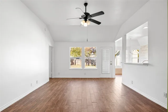 an empty room with wooden floor chandelier fan and windows