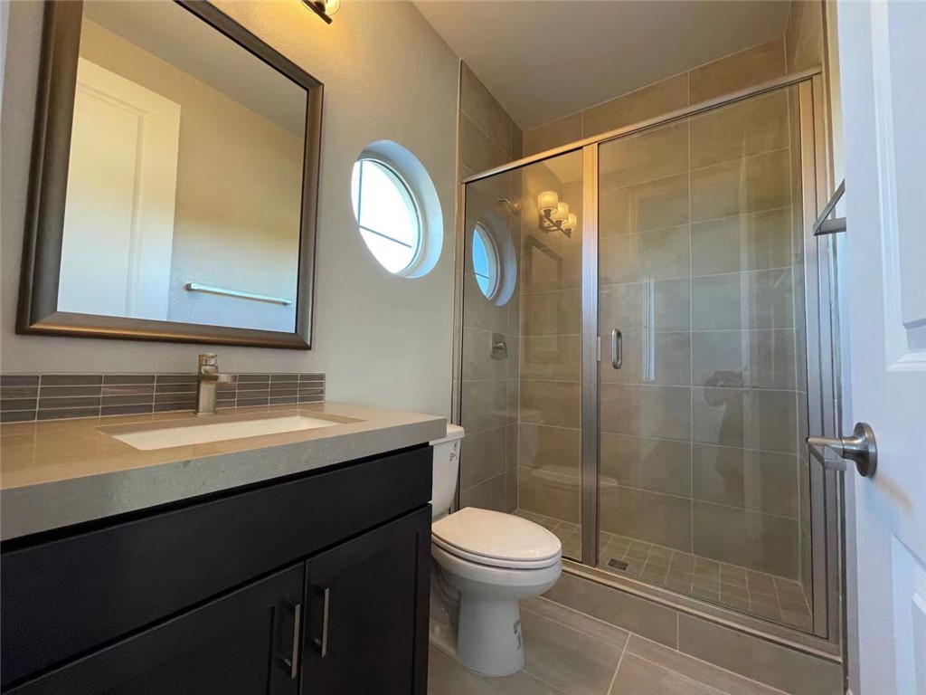 11 Rancho Maria Street Las Vegas, NV 89148 - Photo 24 of 27 Tiled walk-in shower and stone-topped vanity define this modern bathroom with round windows.