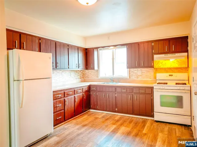 a kitchen with stainless steel appliances granite countertop a refrigerator a sink dishwasher and wooden cabinets with wooden floor