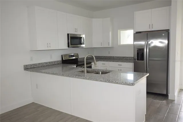 a kitchen with stainless steel appliances granite countertop a sink a microwave a refrigerator and white cabinets