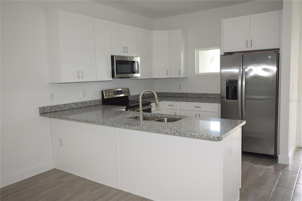 460 Lake Shore Parkway Davenport, FL 33896 - Photo 3 of 27 a kitchen with stainless steel appliances granite countertop a sink a microwave a refrigerator and white cabinets