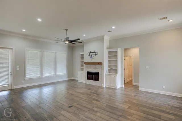 an empty room with wooden floor fireplace and windows