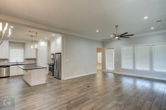 a view of an empty room and kitchen with wooden floor
