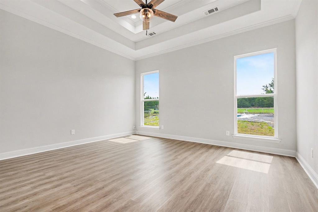 530 P R 491 Leonard, TX 75452 - Photo 17 of 35 Spacious room featuring light-toned wood-finish flooring, two large windows, a tray ceiling with crown molding, and a ceiling fan with integrated lighting