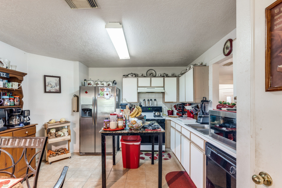 10007 Raymondville Road Houston, TX 77093 - Photo 8 of 19 Two tone kitchen with stainless steel fridge, a textured ceiling, black dishwasher, backsplash, and electric stove