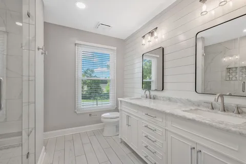 a bathroom with a granite countertop sink a toilet a mirror and window
