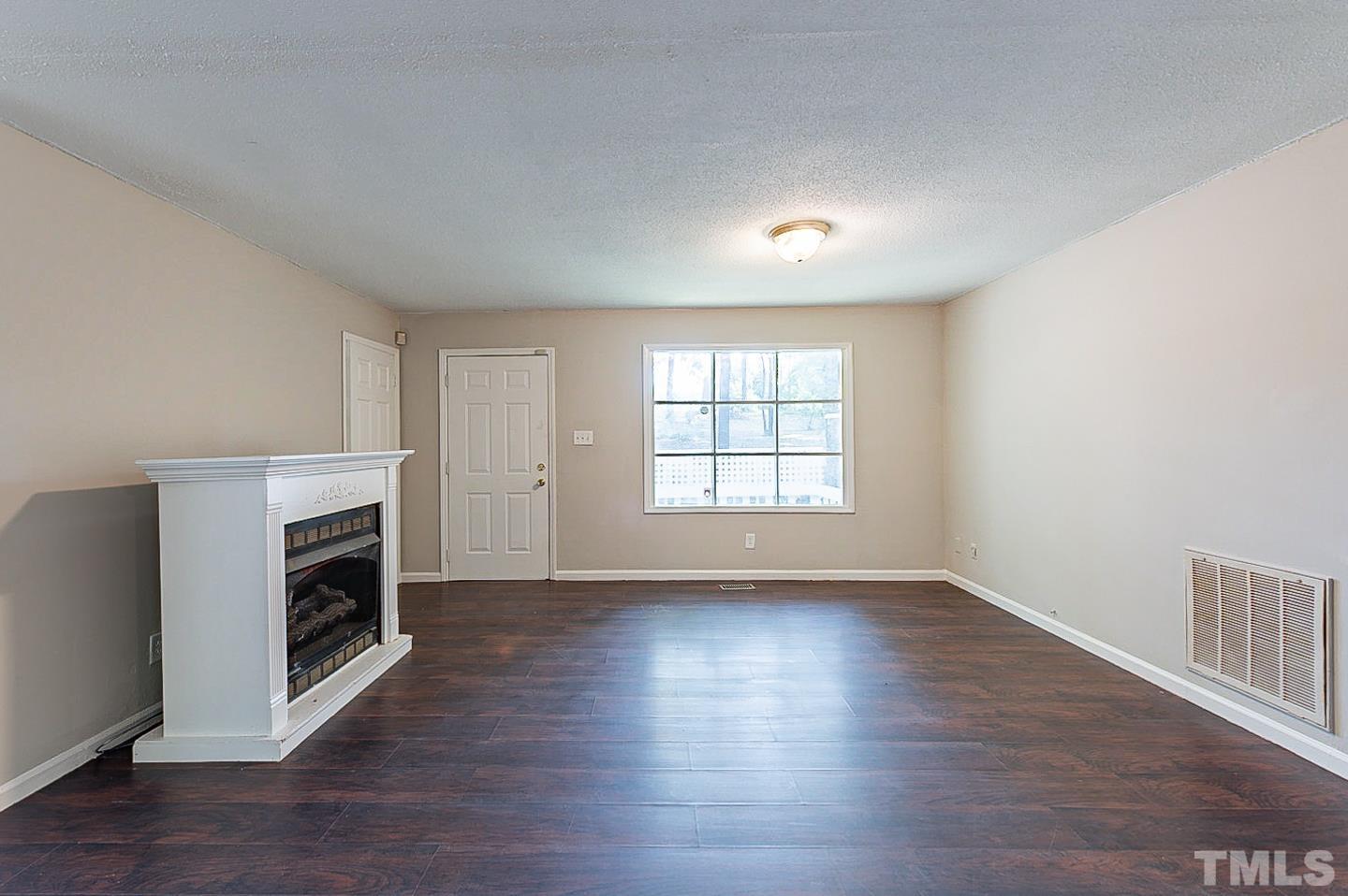 7005 Russell Road Durham, NC 27712 - Photo 3 of 24 an empty room with wooden floor fireplace and windows