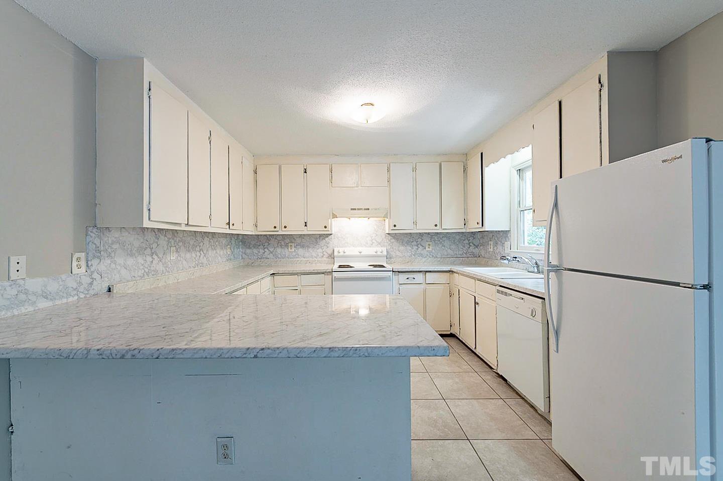7005 Russell Road Durham, NC 27712 - Photo 9 of 24 a kitchen with granite countertop a refrigerator a sink and white cabinets