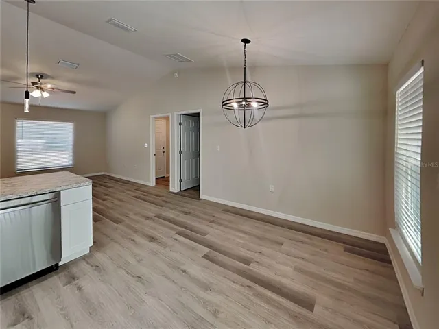 an empty room with wooden floor chandelier and windows