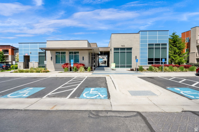 7713 Navarro View Court Midvale, UT 84047 - Photo 26 of 41 Modern low-rise building featuring light-colored brick facade, blue grid-patterned panels, large storefront windows, and a covered entrance