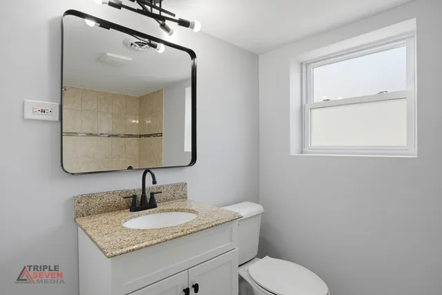a bathroom with a granite countertop sink toilet and mirror