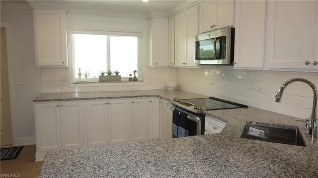 a kitchen with granite countertop a sink a stove top oven and cabinetry