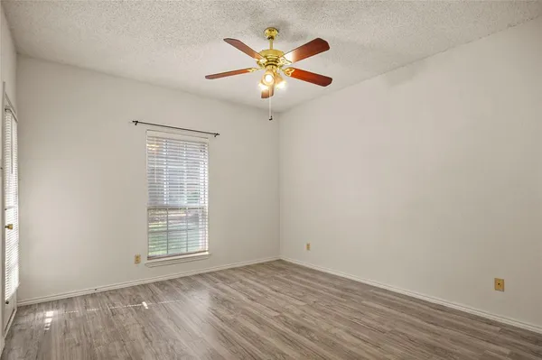 an empty room with wooden floor fan and windows