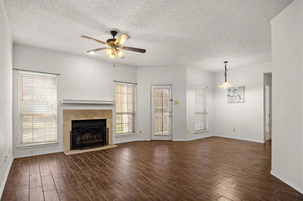 an empty room with wooden floor fireplace fan and windows