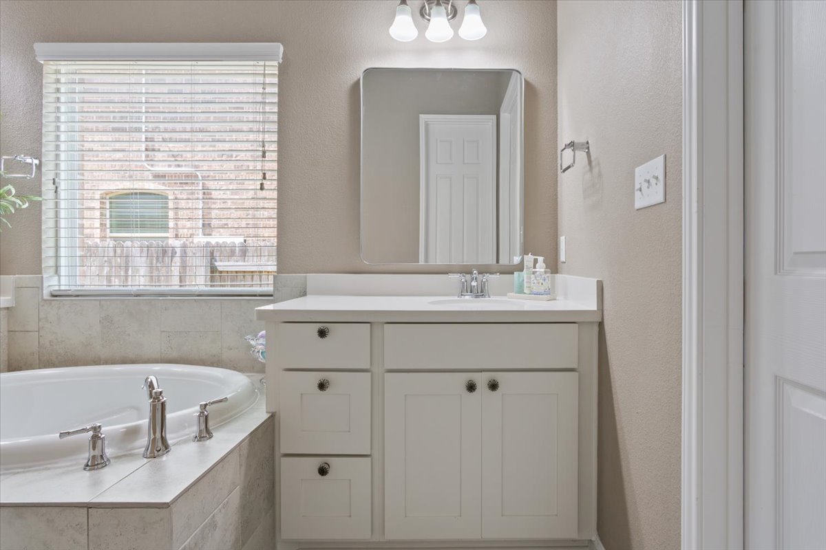 424 Millard Street Georgetown, TX 78628 - Photo 19 of 37 A well-appointed bathroom features a single vanity, a spacious soaking tub, and natural light filtering through window blinds.