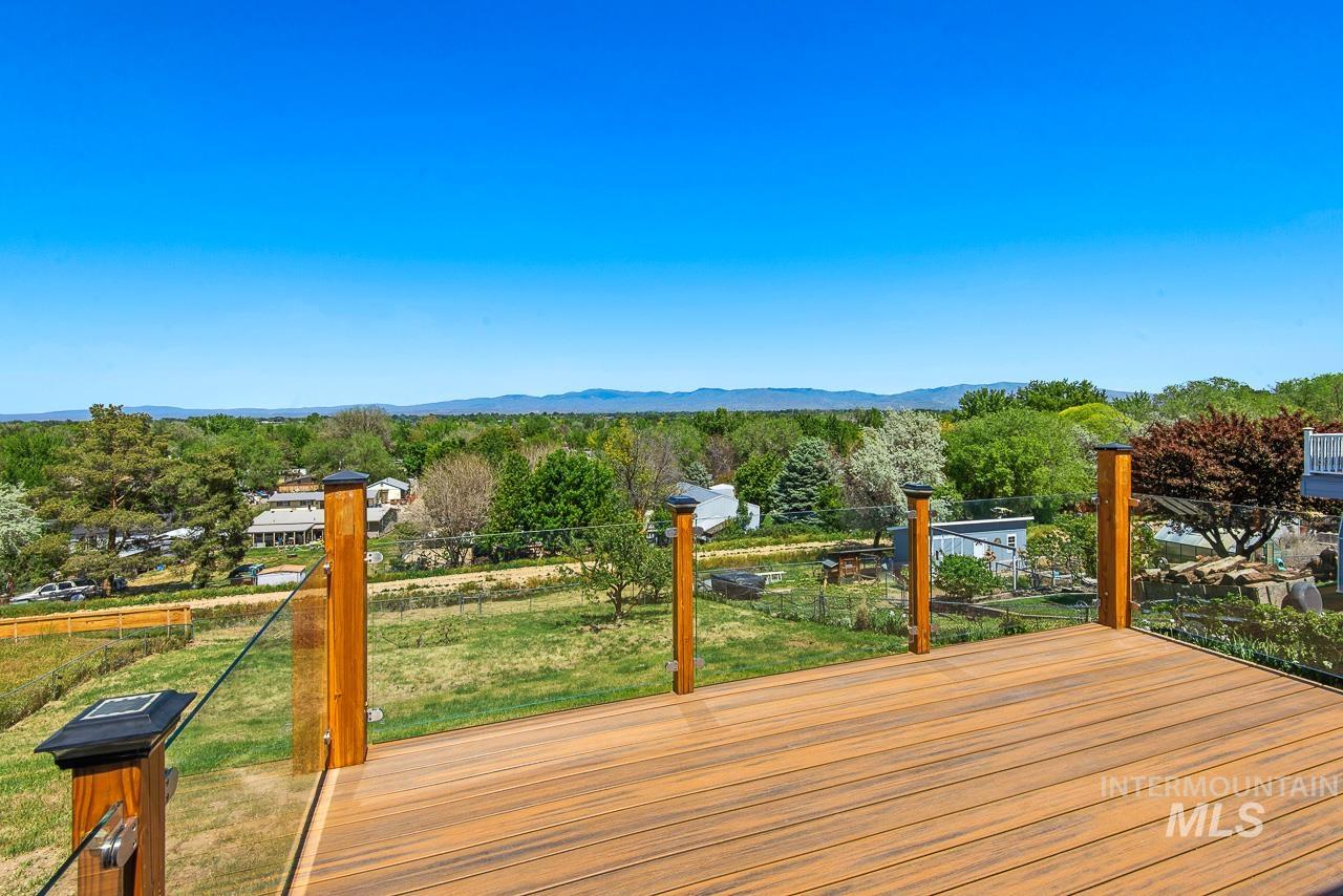 10178 West Fox Ridge Drive Boise, ID 83709 - Photo 8 of 36 Outdoor deck featuring composite decking, clear glass railings, and a wide-ranging tree-lined landscape with mountains in the background