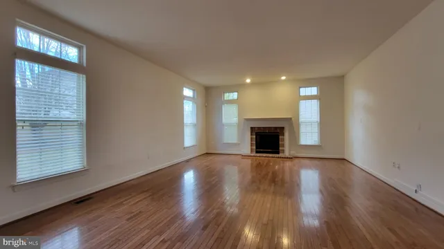 a view of an empty room with wooden floor fireplace and a window