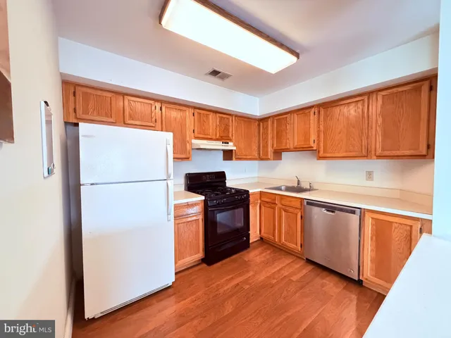 a kitchen with granite countertop wooden floors a stove a sink and a refrigerator