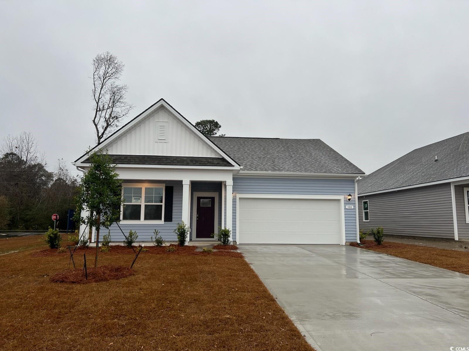 View of front facade with board and batten siding, concrete driveway, a shingled roof, covered porch, and a garage
