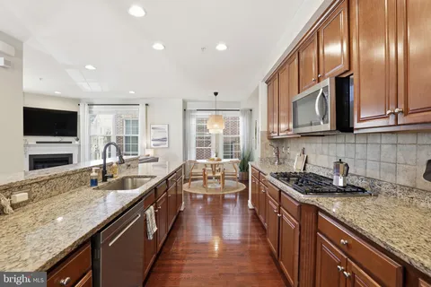 a kitchen with stainless steel appliances granite countertop wooden cabinets a sink and dishwasher a stove top oven with wooden floor